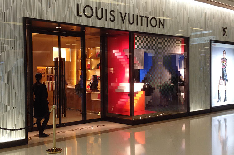 People walk past a Louis Vuitton store at Siam Paragon shopping
